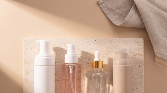 Four VERMELI skincare vessels arranged in ritual order on a travertine slab in warm afternoon light, with folded linen